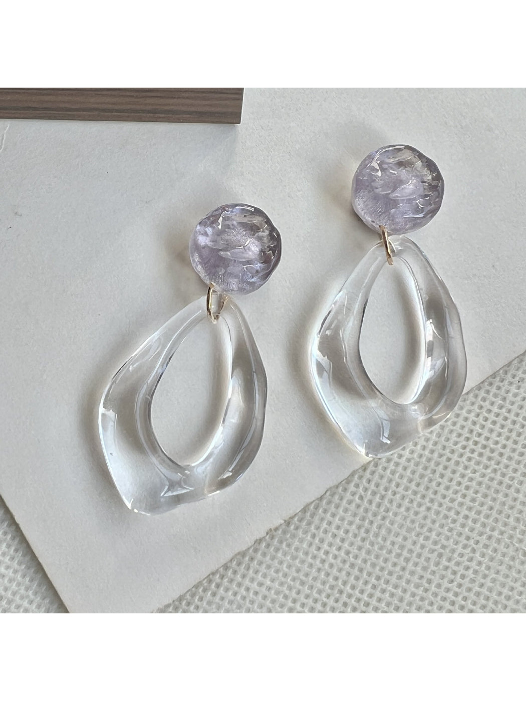 Earwish clear teardrop hoop earrings displayed hanging on a stand