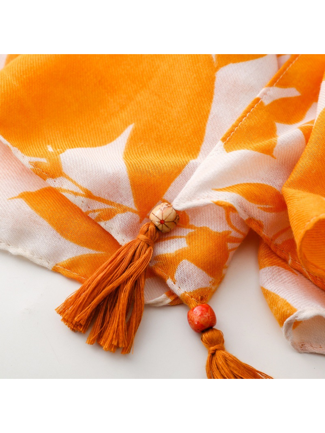 Close-up of two orange tassels and decorative beads on the Floral scarf