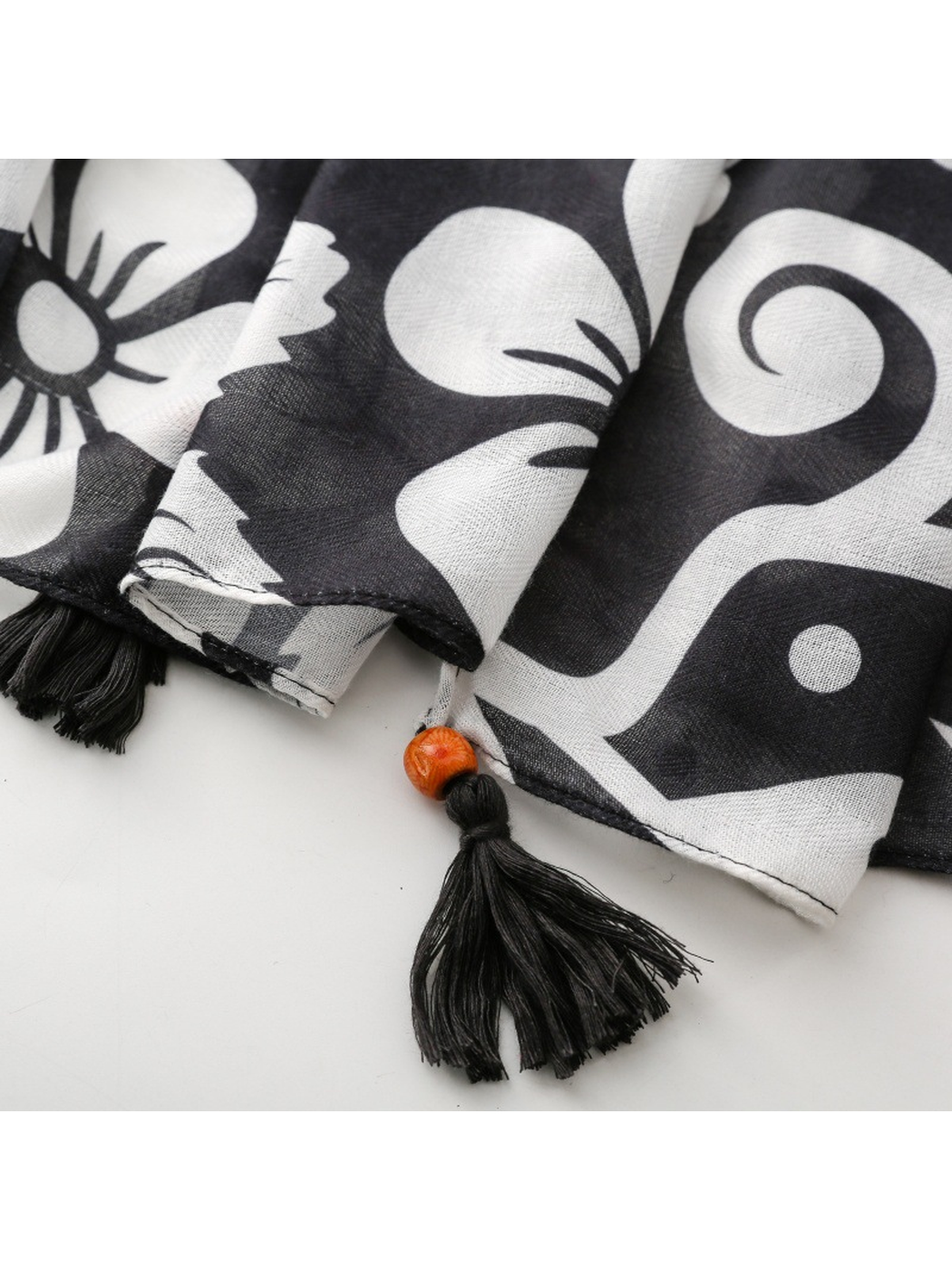 Close-up of a black corner tassel, orange-toned bead and stitched motif-print hem