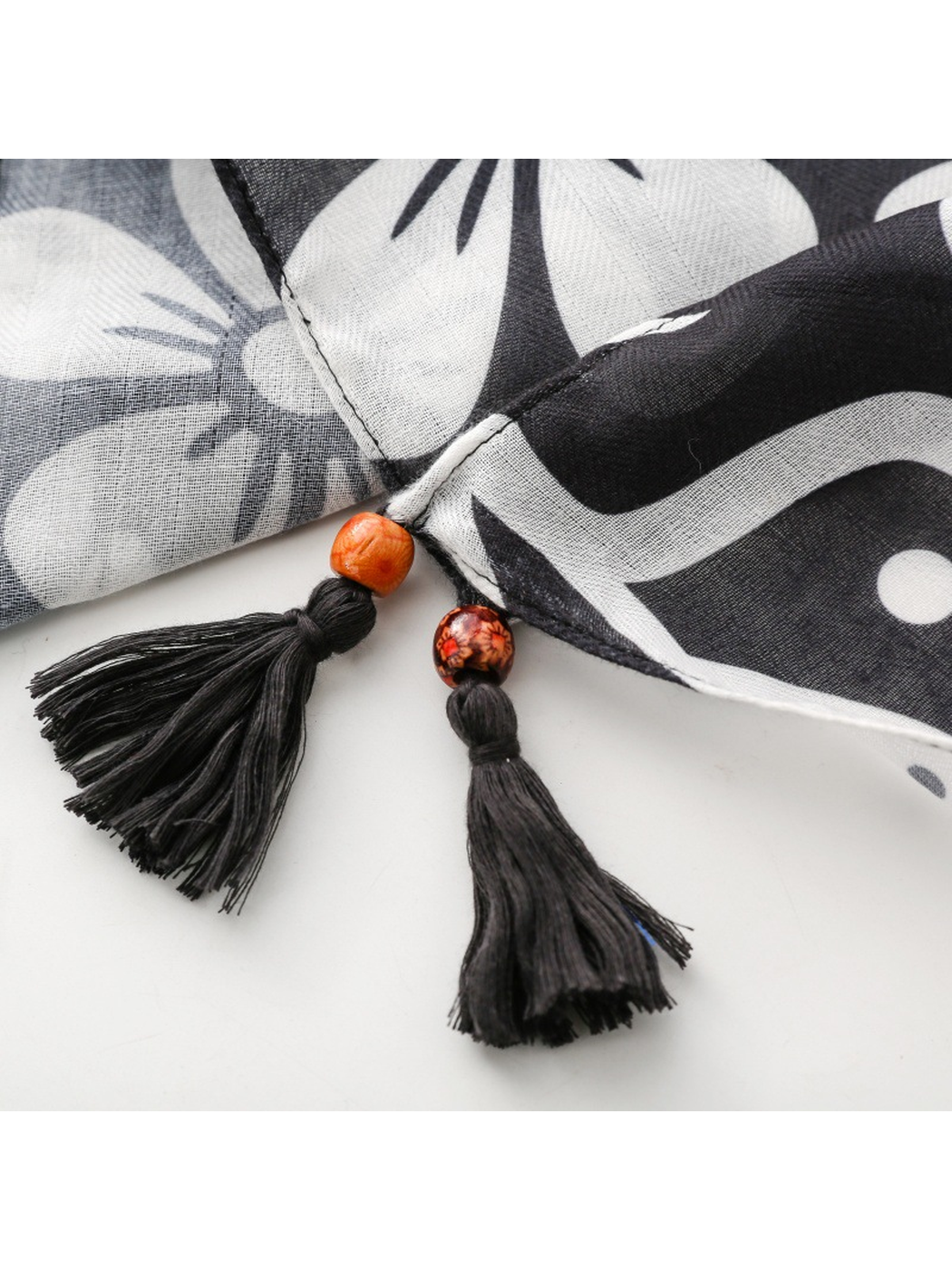 Close-up of two black tassels, orange-toned beads and overlapping scarf corners